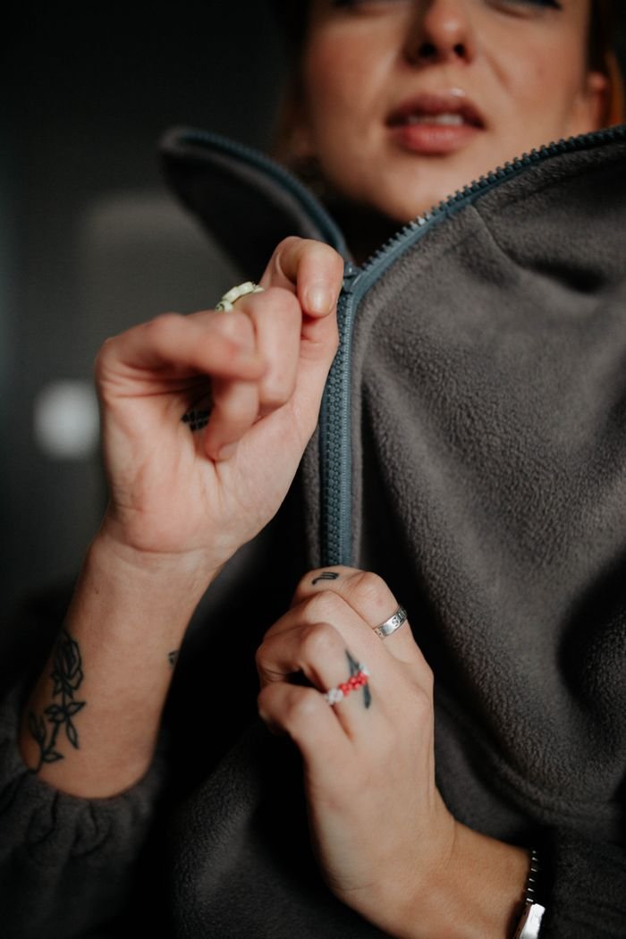 Close-up of a Caucasian woman zipping a fleece jacket, highlighting hands and tattoos.