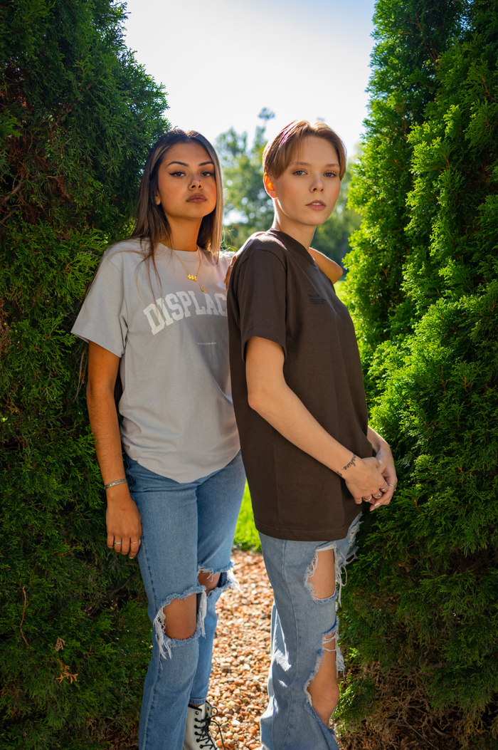Home Two young women pose in casual outfits surrounded by greenery, exuding a fresh and trendy vibe.